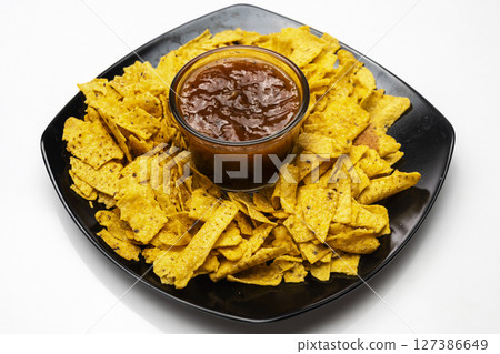 Nachos tortilla chips on the black plate with salsa barbecue sauce in a bowl on a white background. Food and snacks concept 127386649
