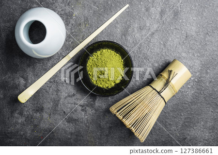 Matcha green tea powder in the black bowl and a traditional bamboo brush whisk with a spoon on a black table. Accessories for making matcha green tea. Top view 127386661