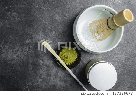 Matcha green tea powder in the black bowl with a wooden spoon and a traditional bamboo brush whisk in an empty bowl on a black table. Accessories for making matcha green tea. Top view 127386678