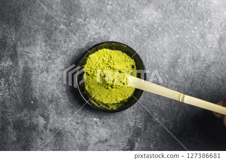 Matcha green tea powder in the black bowl with a traditional bamboo spoon or chashaku on a black table. Accessories for making matcha green tea. Top view 127386681