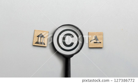 Magnifying glass with copyright logo and icon of law on wooden cubes. Concept of digital copyright and patent, intellectual assets and property, legal protection Magnifying glass with copyright logo and icon of law on wooden cubes. Concept of digital copyright and patent, intellectual assets and property, legal protection 127386772