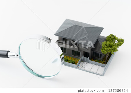 Magnifying glass and miniature detached house on white background 127386834