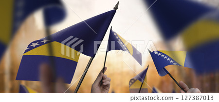 Bosnia and Herzegovina flags in their hands on a blurred urban background 127387013