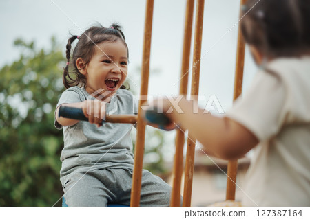 cheerful toddler girl playing on double swing with freind at outdoor playground 127387164