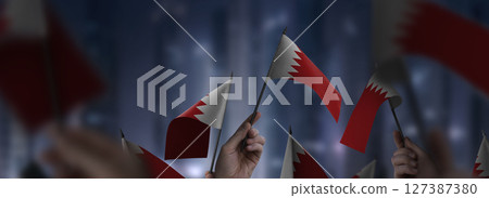 Bahrain flags in their hands on a blurred urban background Bahrain flags in their hands on a blurred urban background 127387380