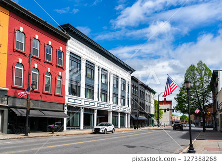 A row of red, white, and gray 19th-century storefronts lines Water Street in Augusta, Maine, United States, where American flags flutter beneath a bright spring sky. A row of red, white, and gray 19th-century storefronts lines Water Street in Augusta, Maine, United States, where American flags flutter beneath a bright spring sky. 127388268