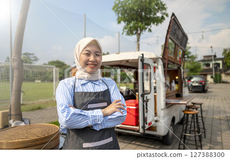 Indonesian southeast asian chinese muslim female barista in hijab standing with confidence in front of her coffee shop. A small business of a coffee shop or cafe on a truck Indonesian southeast asian chinese muslim female barista in hijab standing with confidence in front of her coffee shop. A small business of a coffee shop or cafe on a truck 127388300