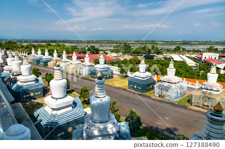 Rows of white stupas line a quiet pathway at Fo Guang Shan Monastery in Kaohsiung, Taiwan, with a traditional Chinese pagoda visible through the trees under a clear blue sky 127388490