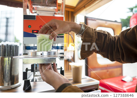 Male barista serving a drink at a table. A small business of a coffee shop or cafe on a truck Male barista serving a drink at a table. A small business of a coffee shop or cafe on a truck 127388646