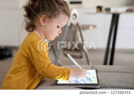 Toddler girl happily drawing on a digital tablet. Relaxed home atmosphere and imaginative play Toddler girl happily drawing on a digital tablet. Relaxed home atmosphere and imaginative play 127390341