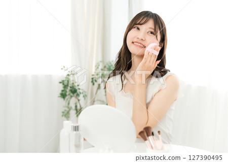 Smiling Asian woman applying foundation powder makeup 127390495