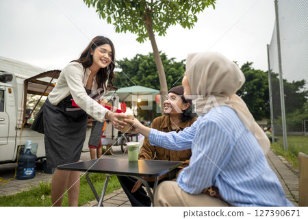 Indonesian southeast chinese asian female waiter serving food and beverage order to chinese muslim woman and man couple customer. A small business on a truck 127390671