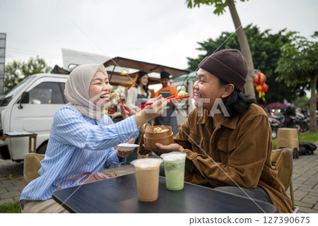 Couple of Indonesian southeast asian man and chinese muslim woman enjoys eating their food and drink in the table park. A small business of a food truck 127390675
