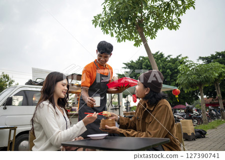 Indonesian southeast asian male waiter serving food order to chinese female and man couple customer. A small business on a truck 127390741