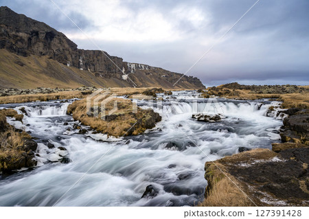 Panoramic view of the cliff and flowing rushing water on the river in Kirkjubaejarklaustur, Iceland. Nature, travel, winter background, or wallpaper 127391428