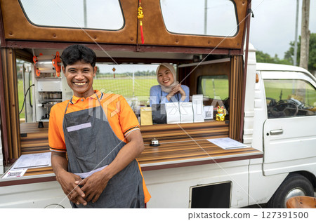 Indonesian southeast asian male and a Chinese muslim female in hijab couple baristas with confidence in their coffee shop. A small business of a coffee shop or cafe on a truck 127391500