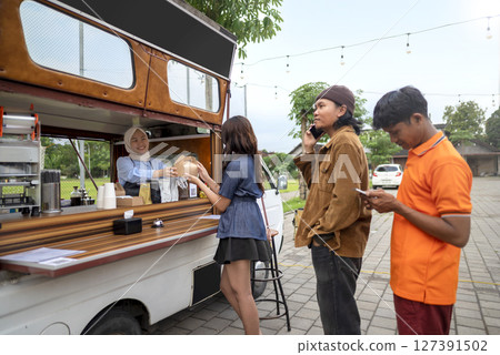 Chinese muslim female in a hijab waiter serving food to Indonesian southeast asian customers. A small business on a truck Chinese muslim female in a hijab waiter serving food to Indonesian southeast asian customers. A small business on a truck 127391502