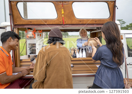 Chinese muslim female in a hijab waiter serving food to Indonesian southeast asian customers. A small business on a truck Chinese muslim female in a hijab waiter serving food to Indonesian southeast asian customers. A small business on a truck 127391503