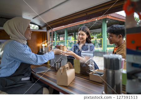 Indonesian southeast asian chinese muslim female waiter in hijab serving food to customers. A small business on a truck 127391513