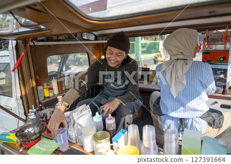 Indonesian southeast asian male and a Chinese muslim female in hijab couple baristas preparing their coffee shop before opening the order. A small business of a coffee shop or cafe on a truck Indonesian southeast asian male and a Chinese muslim female in hijab couple baristas preparing their coffee shop before opening the order. A small business of a coffee shop or cafe on a truck 127391664