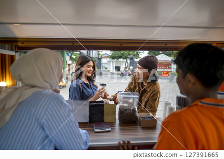 Indonesian southeast asian male and a Chinese muslim female in hijab couple baristas serving drinks and snacks to customers. A small business of a coffee shop or cafe on a truck 127391665