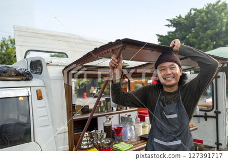 Indonesian southeast asian male barista standing with confidence in front of his coffee shop. A small business of a coffee shop or cafe on a truck 127391717