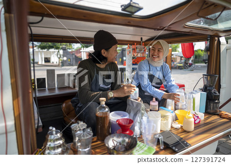 Indonesian southeast asian male and a Chinese muslim female in hijab couple baristas preparing their coffee shop before opening the order. A small business of a coffee shop or cafe on a truck 127391724
