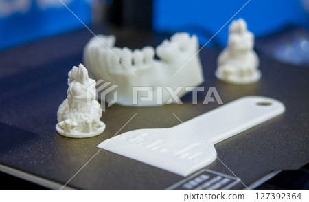 Small white figures made of white plastic printed on a 3D printer on the working surface of a 3D printer close-up. FDM. Concept 3D Printing. Additive modern new progressive technologies 127392364