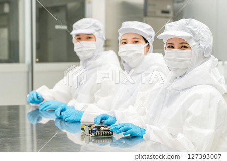 Male and female workers in dustproof clothing handling precision equipment in a clean room 127393007
