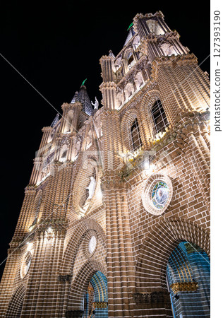 Low-angle night view of Jardin's brick Basilica of the Immaculate Conception, its ornate neo-gothic facade, arches, and soaring spires brilliantly floodlit against a pitch-black sky Low-angle night view of Jardin's brick Basilica of the Immaculate Conception, its ornate neo-gothic facade, arches, and soaring spires brilliantly floodlit against a pitch-black sky 127393190