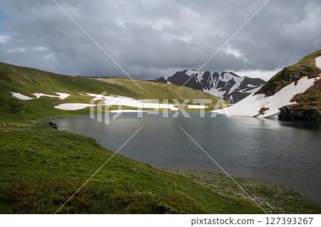 Small alpine lake and green meadows 127393267