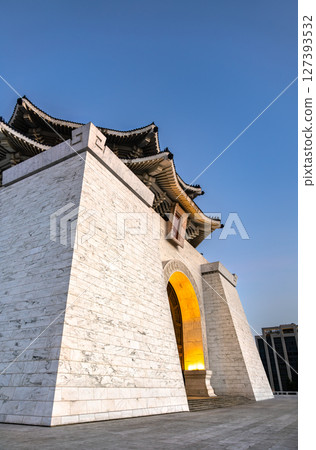 Low-angle perspective of Chiang Kai-Shek Memorial Hall's white-marble base and softly lit arched entrance, rising into a clear evening sky over downtown Taipei in Taiwan 127393532