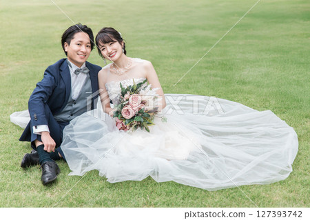 A bride and groom in a wedding dress sitting on the lawn in the garden of the ceremony hall (wedding photo) 127393742