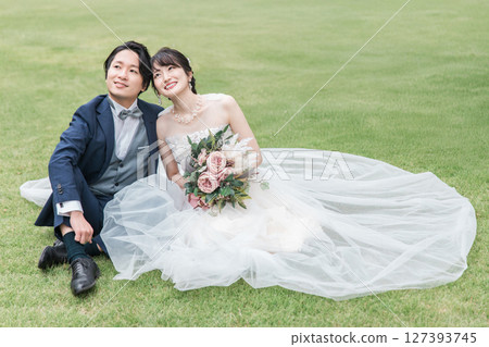 A bride and groom in a wedding dress sitting on the lawn in the garden of the ceremony hall (wedding photo) 127393745
