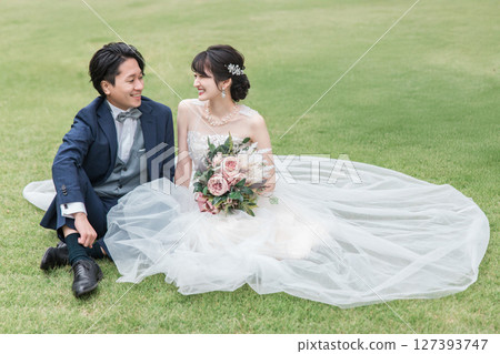 A bride and groom in a wedding dress sitting on the lawn in the garden of the ceremony hall (wedding photo) 127393747