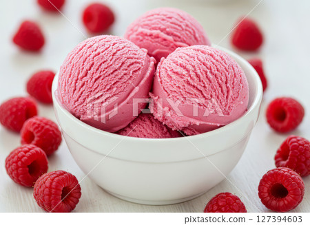 Close-up of a white bowl filled with three scoops of raspberry ice cream, garnished with a raspberry berries.  127394603