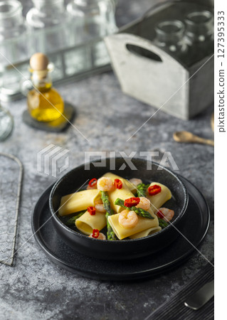 Paccheri pasta with shrimps, asparagus and chili pepper resting on a dark plate Paccheri pasta with shrimps, asparagus and chili pepper resting on a dark plate 127395333