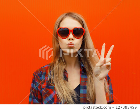 Portrait of beautiful cute blonde young woman blowing a kiss with red heart sunglasses 127395459