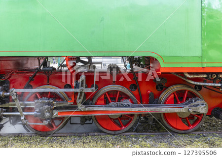 Red wheels and driving rods of a vintage green steam locomotive emitting steam 127395506