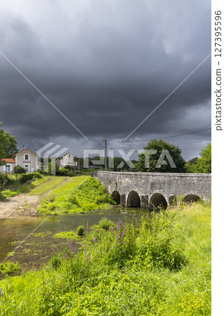 Old stone bridge crossing shallow river under stormy sky in Thorey sur Ouche, France Old stone bridge crossing shallow river under stormy sky in Thorey sur Ouche, France 127395596