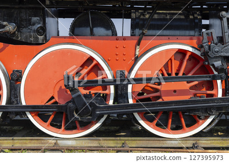 Red and black wheels of an old steam locomotive standing on rails 127395973