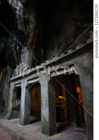 Stone entrance to cave temple in Marble Mountains with floral offerings, Sacred cave shrine with stone columns in Marble Mountains Vietnam 127396239