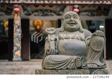 Hotei Buddha statue with lotus base at temple entrance with warm light, Sacred sculpture of Hotei in front of ornate temple with spiritual ambiance 127396240
