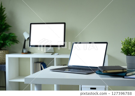 Minimalist home office workspace with laptop and desktop monitor featuring blank white screens Minimalist home office workspace with laptop and desktop monitor featuring blank white screens 127396788