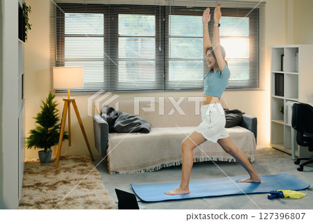 Young woman practicing yoga in warrior pose on mat at home during morning workout 127396807