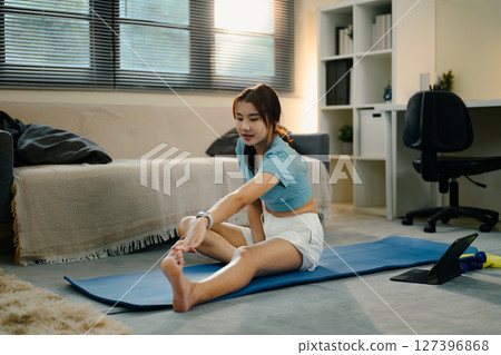 Young woman stretching on a yoga mat at home during a morning fitness routine Young woman stretching on a yoga mat at home during a morning fitness routine 127396868