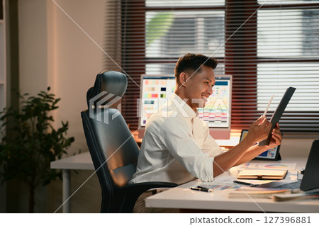 Graphic designer working at desk, analyzing color schemes on a large desktop monitor and tablet 127396881