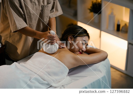 Therapist using a traditional herbal ball to relieve shoulder tension. Wellness concept 127396882