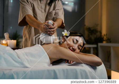 Peaceful woman receiving spa treatment with herbal pouch on back. Wellness concept 127396889