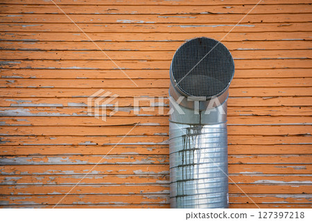 Industrial Ventilation Pipe on Weathered Wooden Wall with Peeling Orange Paint Industrial Ventilation Pipe on Weathered Wooden Wall with Peeling Orange Paint 127397218